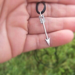 May include: A silver arrow pendant necklace on a black cord. The arrow is detailed with lines and a pointed tip.