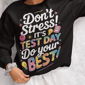 Könnte beinhalten: Schwarzes Sweatshirt mit dem Text "Don't Stress! It's Test Day Do your BEST" in einem farbenfrohen, Batik-Stil. Das Design beinhaltet ein Smiley, Glühbirnen, ein Notizbuch und einen Bleistift. Unten steht "HIGH-QUALITY 300DPI PNG".