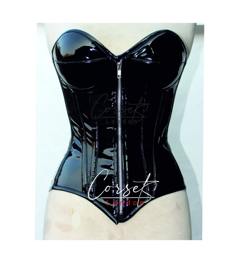 May include: A black patent leather corset with a front zip fastening. The corset has a sweetheart neckline and boning along the sides. The brand name "Corset London" is printed on the front of the corset.