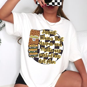 Könnte beinhalten: Weißes T-Shirt mit einem Grafikdesign mit einer Malzgetränkedose, Arepas und dem Text "Suspect Claims That Arepas and Malta are part of her diet plan". Das Design enthält einen schwarz-weiß karierten Kreis.