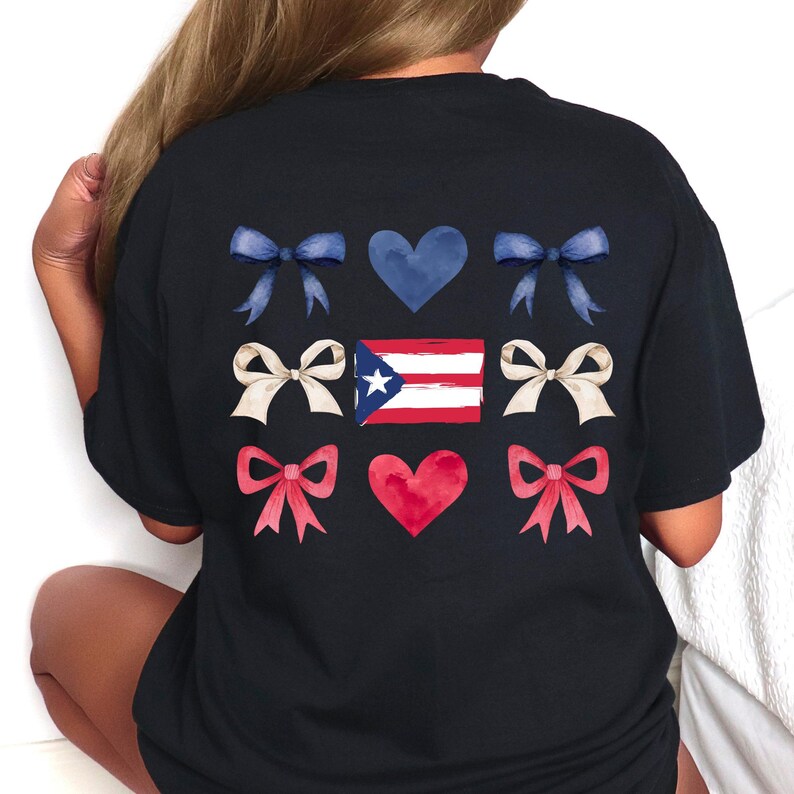 May include: Black t-shirt featuring a design with blue bows, white bows, and red bows, along with blue and red hearts. The Puerto Rican flag is in the center of the design. The shirt is a comfortable, casual style.