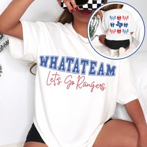 Könnte beinhalten: Weißes T-Shirt mit dem Text "WHATATEAM" in blauen Blockbuchstaben und "Let's Go Rangers" in roter Schrift. Ein kleines Bild zeigt die Rückseite des Shirts mit einer Texas-Umrisslinie und "WOW"-Grafiken. Das Shirt ist ein lässiges Fan-Themen-Kleidungsstück.