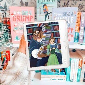 Könnte beinhalten: Ein weißer Kobo-E-Reader mit einer Illustration von dem Biest und Belle aus Die Schöne und das Biest. Das Biest hält einen hohen Stapel Bücher, während Belle ein blaues Buch liest. Das Gerät hat einen Bildschirm mit zwei vertikalen Tasten.