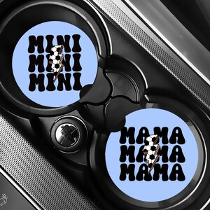 Puede incluir: Dos posavasos de coche azul claro con texto negro y un gr&aacute;fico de bal&oacute;n de f&uacute;tbol. Un posavasos dice "MINI" tres veces, y el otro dice "MAMA" tres veces. Los posavasos est&aacute;n en el portavasos de un coche.