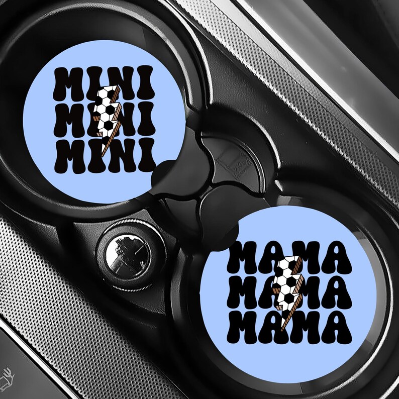 Puede incluir: Dos posavasos de coche azul claro con texto negro y un gr&aacute;fico de bal&oacute;n de f&uacute;tbol. Un posavasos dice "MINI" tres veces, y el otro dice "MAMA" tres veces. Los posavasos est&aacute;n en el portavasos de un coche.