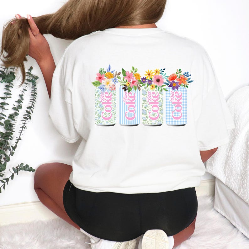 K&ouml;nnte beinhalten: Wei&szlig;es T-Shirt mit einem Design aus vier Diet Coke-Dosen, die jeweils mit Blumen geschm&uuml;ckt sind. Die Dosen zeigen verschiedene Muster: floral, vertikale Streifen und Vichy. Der Text "Diet Coke" ist auf jeder Dose zu sehen.