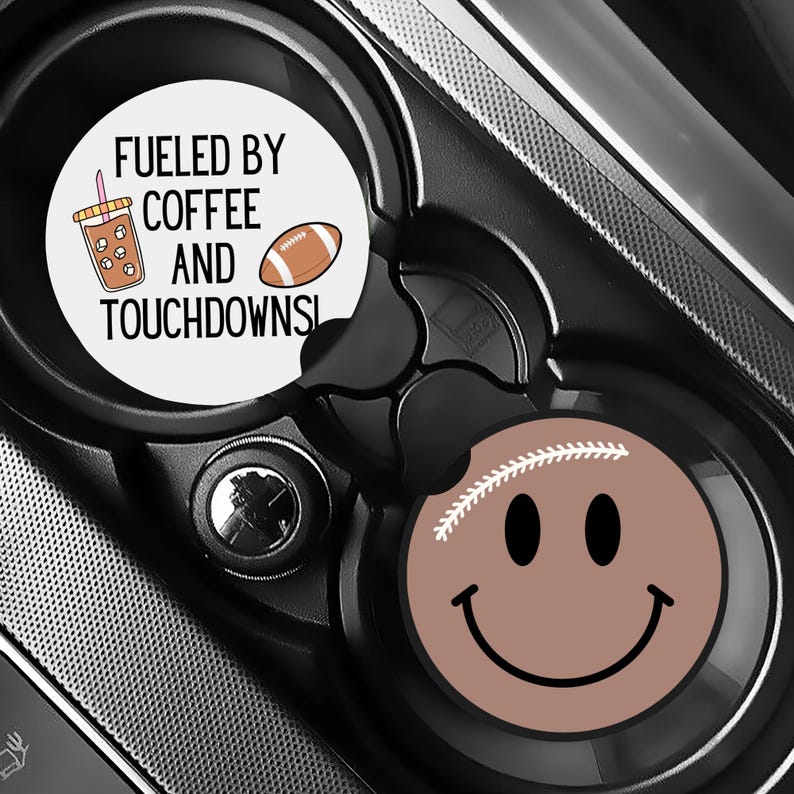 Puede incluir: Dos posavasos para coche con tem&aacute;tica de f&uacute;tbol. Un posavasos tiene el texto "Fueled by Coffee and Touchdowns" con un dibujo de taza de caf&eacute; y bal&oacute;n de f&uacute;tbol. El otro posavasos es una cara sonriente marr&oacute;n con costuras de f&uacute;tbol.