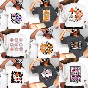 Könnte beinhalten: Eine Auswahl an weißen und grauen T-Shirts mit Halloween-Motiven. Die Designs zeigen Cartoon-Charaktere in Kostümen, Blumenmuster und Texte wie "Coolest Pumpkin in the Patch" und "Let's Go Ghouls."