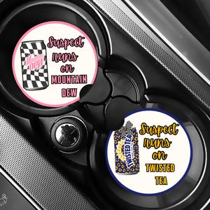 May include: Two car coasters with the text "Suspect runs on MOUNTAIN DEW" and "Suspect runs on TWISTED TEA". One coaster features a Mountain Dew can with a black and white checkered pattern. The other has a Twisted Tea can.