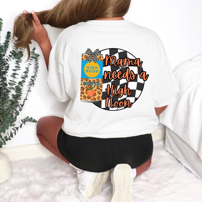 Puede incluir: Camiseta blanca con un dise&ntilde;o gr&aacute;fico que presenta una lata de High Noon con un melocot&oacute;n y el texto "Mama needs a High Noon". El dise&ntilde;o incluye un patr&oacute;n de cuadros blancos y negros y un estampado de leopardo.
