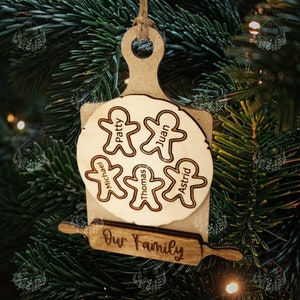 May include: Wooden Christmas ornament shaped like a rolling pin and a gingerbread cookie cutter. The ornament is decorated with the names "Patty", "Juan", "Michael", "Thomas", and "Astrid" and the text "Our Family".
