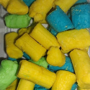 May include: A clear container filled with colorful, cylindrical candies. The candies are in shades of yellow, blue, and green. The candies appear to be coated in a sugary substance.