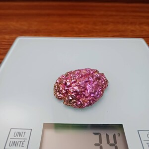 Könnte beinhalten: Ein rosa-goldener, schillernder Kristall mit einem Gewicht von 34 Gramm auf einer digitalen Waage.