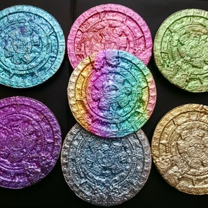 May include: Seven round, iridescent, metallic coasters with a raised design of the Aztec calendar. The coasters are in shades of blue, green, purple, gold, and pink.