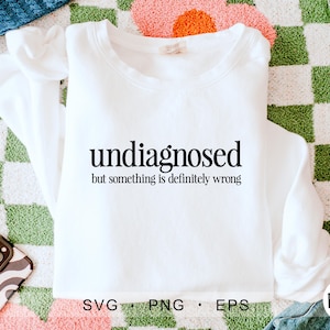 Op de afbeelding: Wit sweatshirt met zwarte tekst die "undiagnosed but something is definitely wrong" luidt.