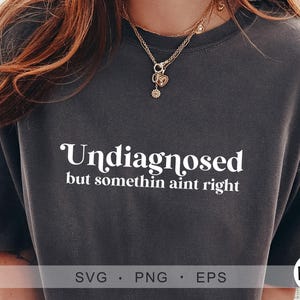 May include: A dark grey t-shirt with the text "Undiagnosed but somethin aint right" in white lettering.