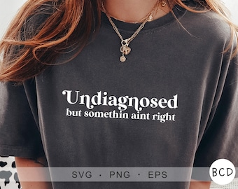 Peut inclure: Un t-shirt gris foncé avec le texte "Undiagnosed but somethin aint right" en lettres blanches.