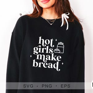Puede incluir: Sudadera negra con texto blanco que dice "hot girls make bread" y una pequeña ilustración de un tarro de pan.