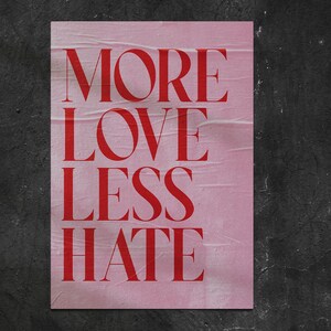 May include: A pink poster with the words "MORE LOVE LESS HATE" in bold red letters. The poster has a distressed, wrinkled texture and is set against a dark, textured background.