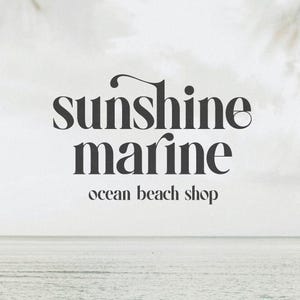 May include: A logo with the words "sunshine marine" in a dark gray, elegant font. Below, the text "ocean beach shop" is in a smaller, lighter font. The background is a soft, neutral color with a blurred image of the ocean.