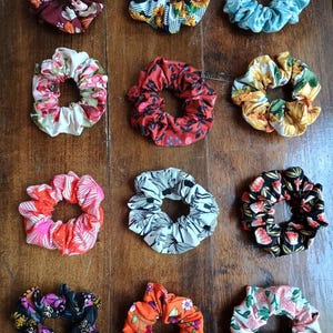 May include: A collection of colorful scrunchies with various floral patterns. The scrunchies are made of fabric and come in a variety of colors, including red, blue, yellow, and orange. The scrunchies are arranged on a wooden surface.
