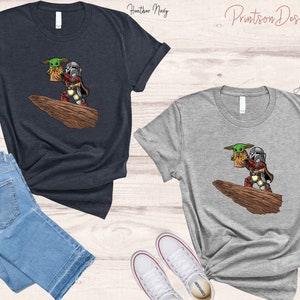 May include: Two t-shirts with a graphic print of a Mandalorian and Grogu, also known as Baby Yoda, standing on a rock. The t-shirts are available in heather navy and athletic grey.