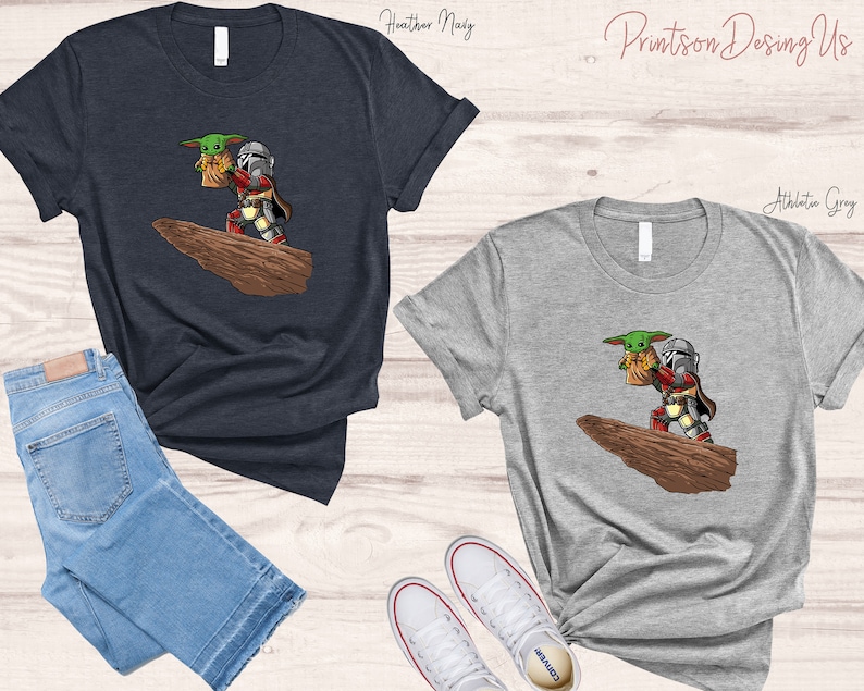May include: Two t-shirts with a graphic print of a Mandalorian and Grogu, also known as Baby Yoda, standing on a rock. The t-shirts are available in heather navy and athletic grey.