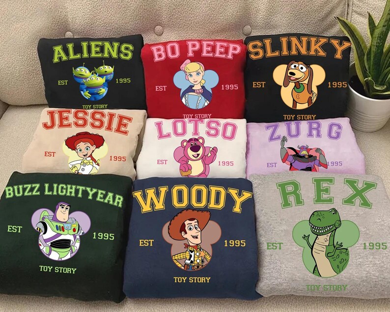 Puede incluir: Nueve sudaderas con dise&ntilde;os de personajes de "Toy Story". Cada sudadera presenta nombres como "Aliens", "Bo Peep" y "Slinky", junto con ilustraciones de personajes y el texto "EST 1995 TOY STORY."