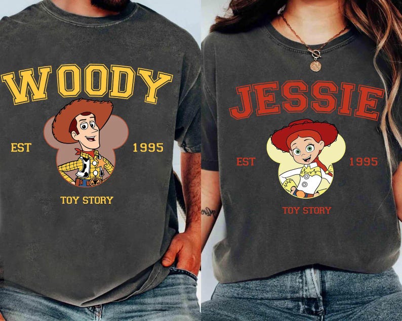 Puede incluir: Dos camisetas gris carb&oacute;n con personajes de Toy Story. Una camiseta muestra "WOODY" en amarillo, con la imagen de Woody, "EST 1995" y "TOY STORY". La otra camiseta muestra "JESSIE" en rojo, con la imagen de Jessie, "EST 1995" y "TOY STORY".