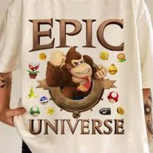 May include: White t-shirt with a brown cartoon gorilla wearing a red bandana and holding a banana. The gorilla is surrounded by video game icons and the words "EPIC UNIVERSE" are printed above and below the gorilla.