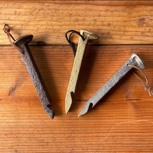 May include: Three metal bottle openers shaped like nails with leather straps. The nail heads are different colours: black, gold, and silver.