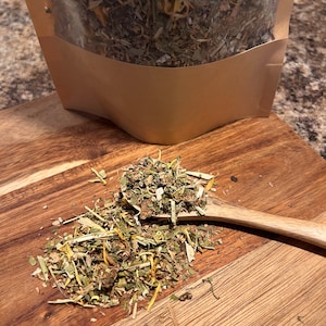 May include: A brown paper bag filled with a blend of dried herbs and flowers. The bag is open and the herbs are spilling out onto a wooden surface.