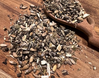 May include: A wooden spoon filled with a mix of dried herbs and seeds, spilling onto a wooden cutting board. The blend includes various shapes and colors, from dark brown seeds to light green leaves, creating a natural, earthy aesthetic.