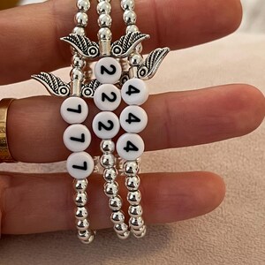 Pu&ograve; includere: Tre braccialetti di perline con perline e ciondoli color argento. Ogni braccialetto ha perline di lettere bianche che compongono i numeri: 777, 222 e 444. I ciondoli sono ali d'angelo.