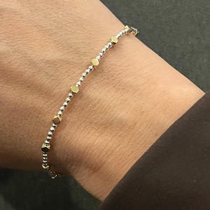 May include: A delicate bracelet with alternating gold hexagonal and small silver round beads. The bracelet is worn on a wrist, highlighting its simple, elegant design. The jewellery is a stylish accessory, perfect for everyday wear.