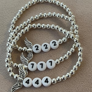 Pu&ograve; includere: Tre braccialetti con perline d'argento. Ogni braccialetto presenta perline bianche con i numeri 222, 777 e 444. Ogni braccialetto ha un ciondolo d'argento con un design ad ala.
