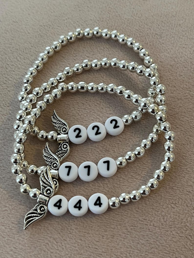 Pu&ograve; includere: Tre braccialetti con perline d'argento. Ogni braccialetto presenta perline bianche con i numeri 222, 777 e 444. Ogni braccialetto ha un ciondolo d'argento con un design ad ala.