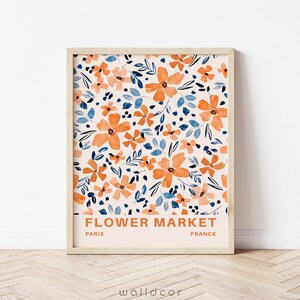 May include: A framed print with a floral pattern in shades of orange, blue, and white. The print has the text "FLOWER MARKET" in orange, "PARIS" in black, and "FRANCE" in black.