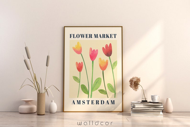 May include: A framed art print with the text "FLOWER MARKET AMSTERDAM" above a watercolor illustration of tulips in shades of red, pink, and yellow. The print is displayed on a light-colored wall, with decorative vases and books nearby.