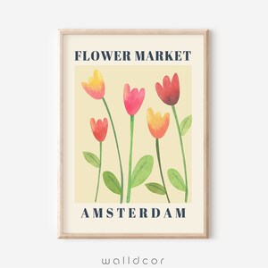 May include: A framed art print featuring a watercolor illustration of colorful tulips. The flowers are in shades of red, pink, and yellow, with green stems and leaves, set against a cream background. The text "FLOWER MARKET AMSTERDAM" is displayed in navy blue.