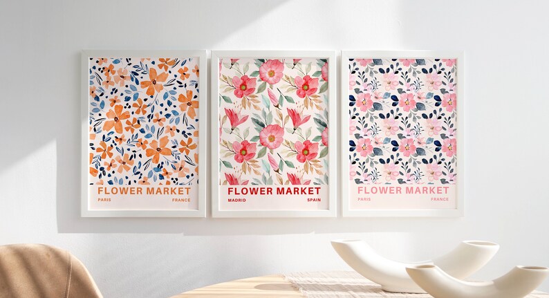 May include: Three framed floral prints with the text "FLOWER MARKET" and the city and country of origin below. The prints feature different floral patterns in shades of pink, orange, and blue.