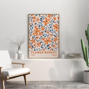May include: A framed print with a floral pattern in shades of orange and blue. The print has the text "FLOWER MARKET" with "PARIS" and "FRANCE" underneath.