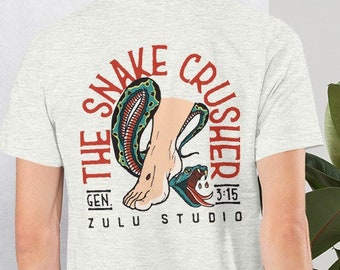 May include: A heather grey t-shirt with a red, white, and blue graphic of a snake being crushed by a foot. The graphic includes the text "The Snake Crusher" and "Gen. 3:15 Zulu Studio".