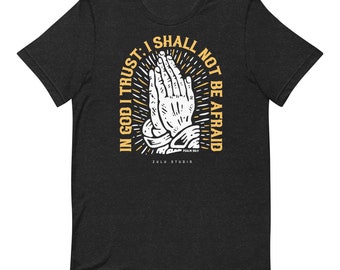 May include: Black t-shirt with a yellow graphic of praying hands and the text "In God I Trust: I Shall Not Be Afraid" with the scripture reference "Psalm 56:11" and the text "Zulu Studio".