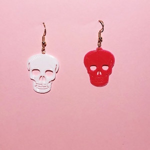 May include: A pair of skull-shaped earrings, one white and one red, with gold hooks.