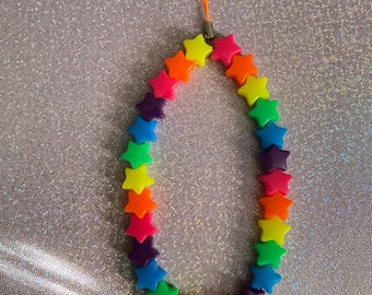 May include: A rainbow-colored star-shaped phone charm with a bright orange lanyard. The charm is made of plastic and has a silver metal ring.