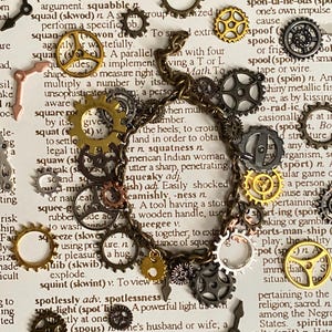 May include: A steampunk-style bracelet featuring various small metal gears in gold, silver, and bronze tones. The bracelet is set against a backdrop of vintage dictionary pages, creating a unique, industrial aesthetic.