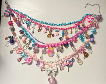 May include: A multi-layered charm necklace featuring bright plastic chains in turquoise, hot pink, purple, and white. The necklace is adorned with numerous colorful charms including lollipops, stars, bows, hearts, a cupcake, and various beads.