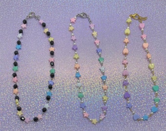 May include: Three necklaces with pastel colored star and heart charms. The necklaces are on a sparkly purple background.