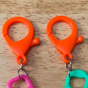 May include: Two orange plastic clasps with silver metal rings attached to pink and green plastic loops.